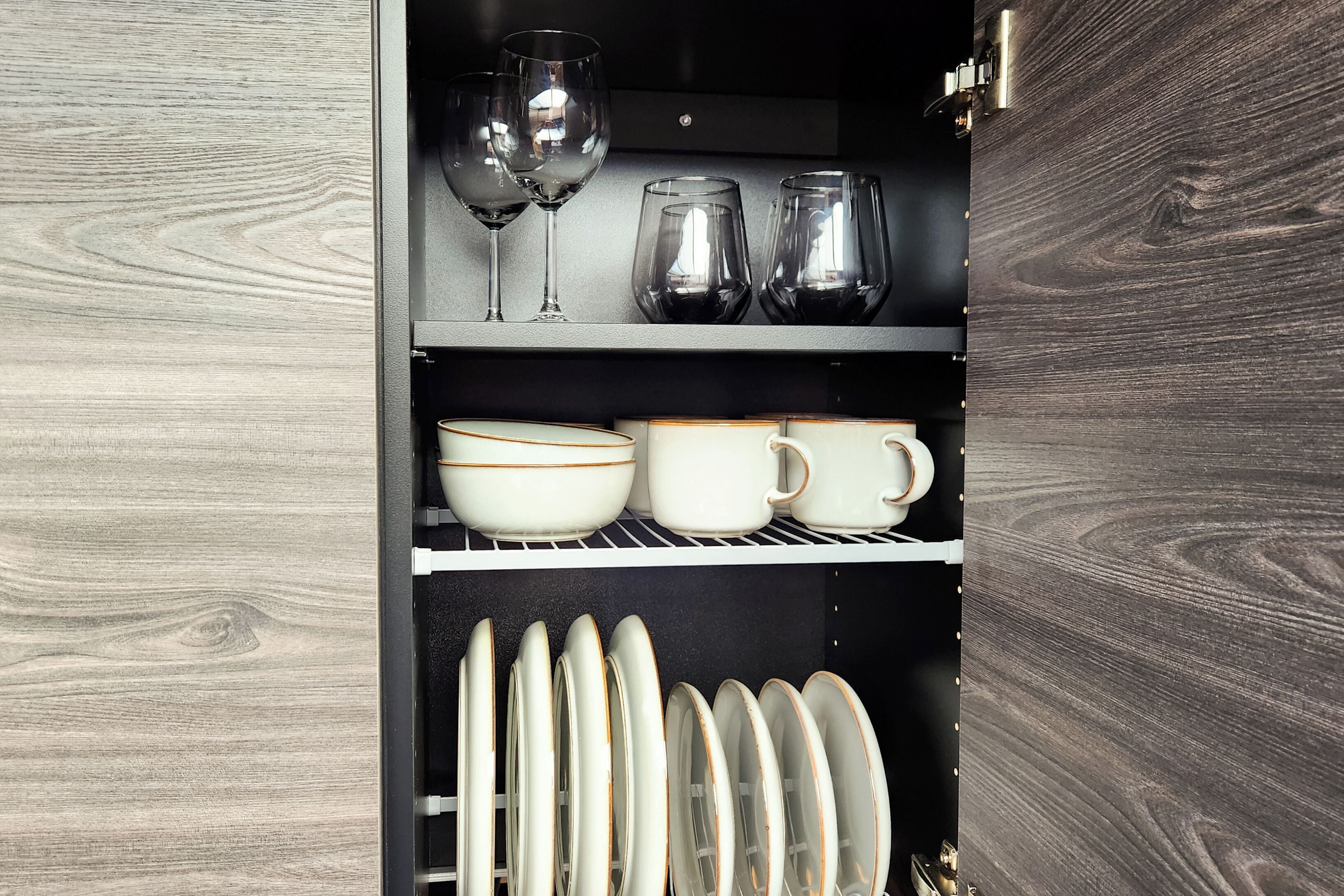 Un armario de cocina con estantes que contienen copas de vino, tazas, cuencos y platos.