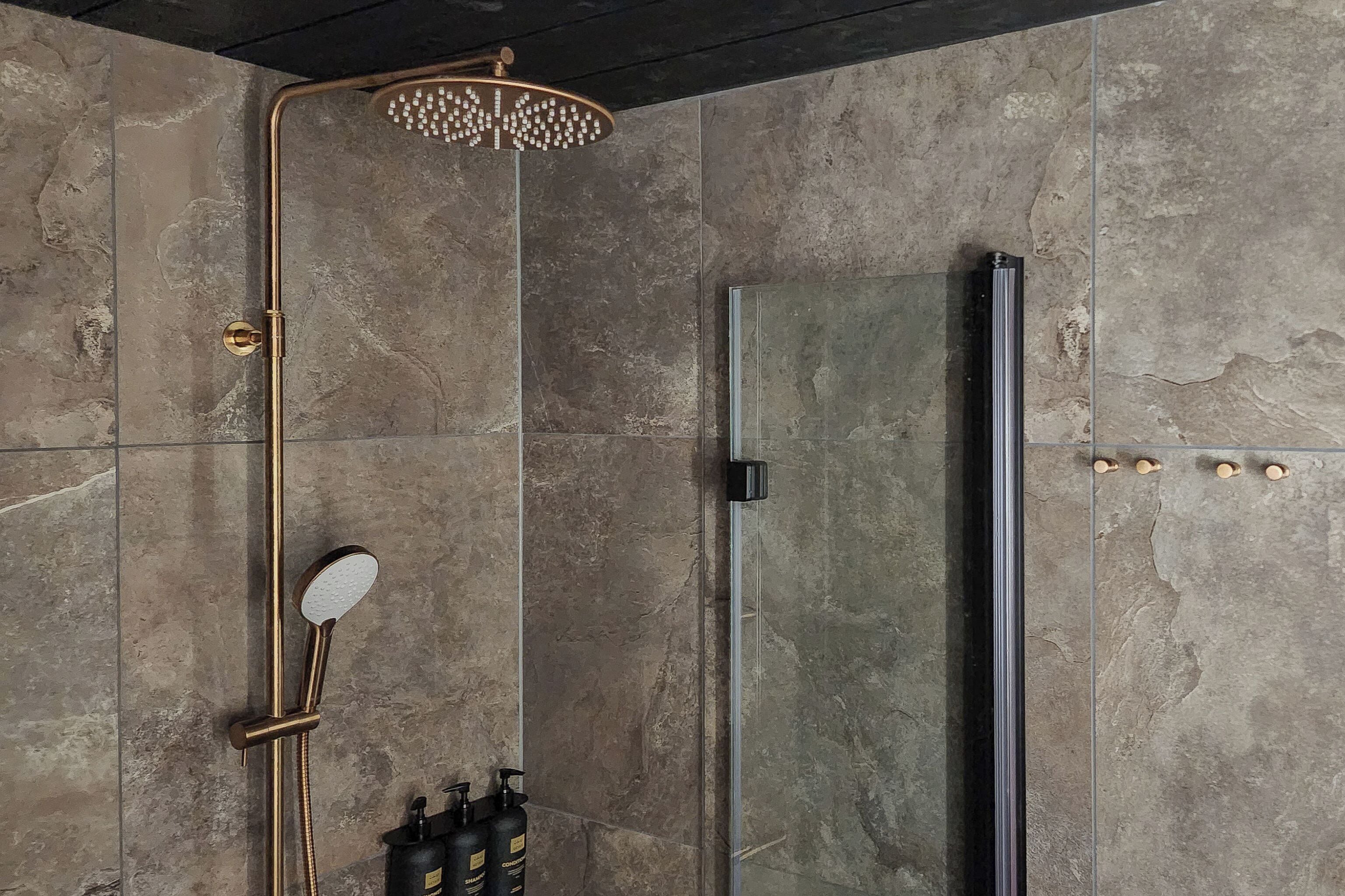 A modern shower with a gold fixture and a glass enclosure.
