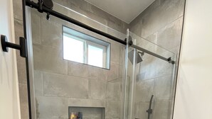 Une salle de bain moderne avec une douche à parois de verre, des toilettes et une petite étagère contenant des articles de toilette.