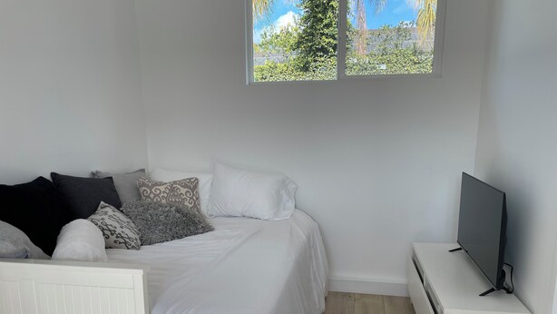 Une chambre à coucher avec un lit, des oreillers, un téléviseur posé sur un meuble et une fenêtre donnant sur un paysage verdoyant.