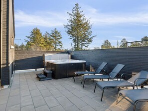 Une terrasse extérieure dotée d’un jacuzzi, de chaises longues et d’une clôture en bois.