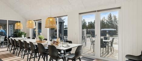 Un espace de salle à manger moderne avec une longue table, des chaises noires et des luminaires suspendus.