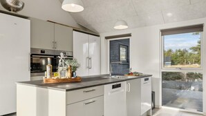 Une cuisine moderne avec des meubles blancs, des appareils en acier inoxydable et une grande fenêtre donnant sur l’extérieur.