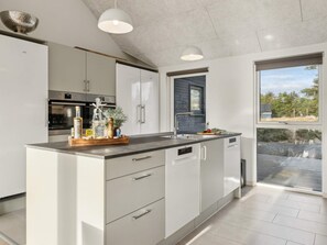 Une cuisine moderne avec des meubles blancs, des appareils en acier inoxydable et une grande fenêtre donnant sur l’extérieur.