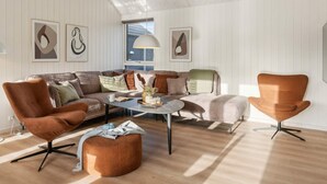 Un salon moderne doté d’un haut plafond, d’un canapé d’angle, d’une table basse et de deux fauteuils.