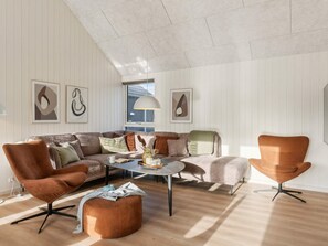 Un salon moderne doté d’un haut plafond, d’un canapé d’angle, d’une table basse et de deux fauteuils.