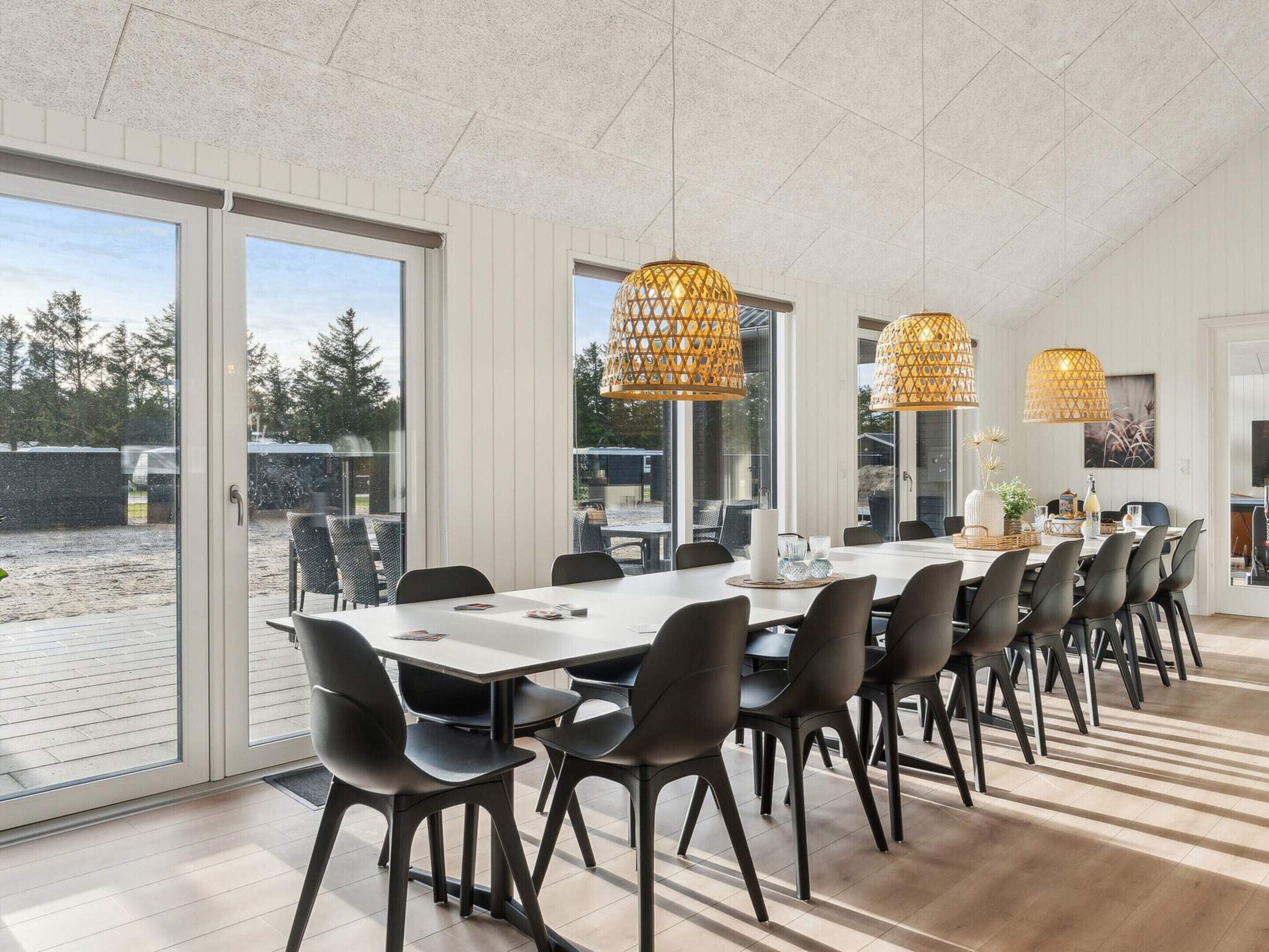 A modern dining area with a long table, black chairs, and large woven pendant lights.