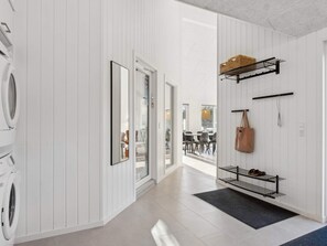 A laundry area with a washing machine, a mirror, and a shoe rack with a handbag. - 5 Star Holiday Home in Vejers Strand (Vejers Strand)