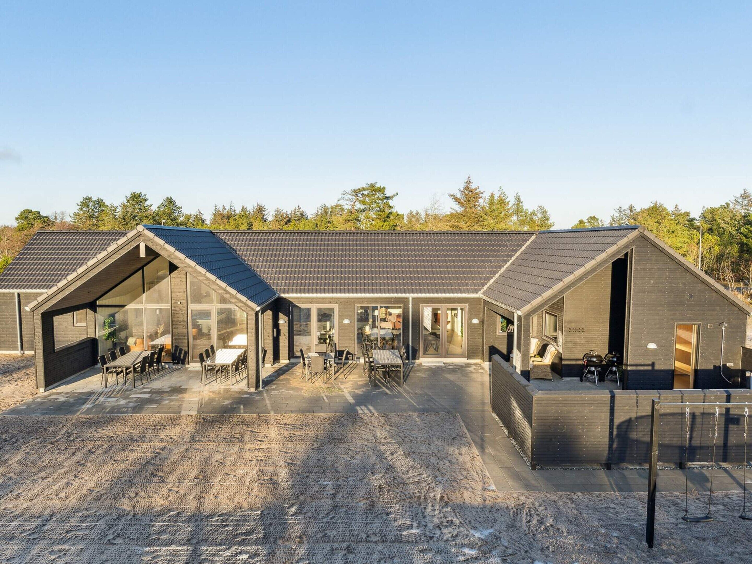 A modern building with large glass windows, a covered outdoor seating area, and a gravel driveway.