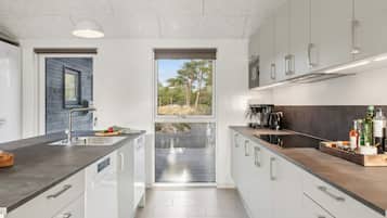 Cozinha moderna com armários brancos, bancada escura e vista para o exterior através de uma porta deslizante.
