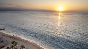 A beach with a pool area, palm trees, and a sunset over the ocean.