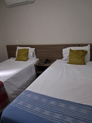 Ein Hotelzimmer mit zwei Einzelbetten, jedes mit weißer Bettwäsche und einem gemusterten Kissen. Ein Nachttisch mit Telefon und Steckdose ist vorhanden.