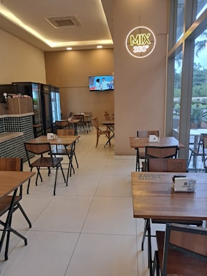 Ein Restaurantinneres mit Tischen, Stühlen, einem an der Wand befestigten Fernseher und einem Neonlicht.