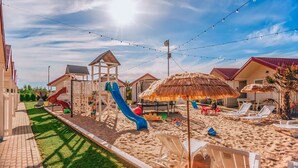 A beachside playground with slides, a playhouse, and beach chairs.