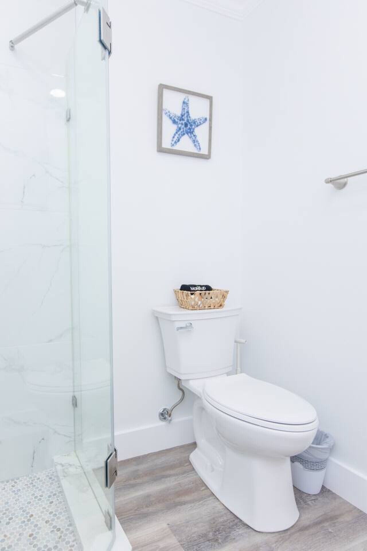 Un baño con cabina de ducha de vidrio, inodoro y una decoración de estrella de mar enmarcada en la pared.