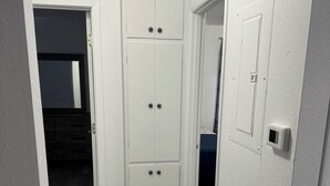 Un pasillo estrecho con un armario blanco, una puerta que da a otra habitación y un termostato en la pared.