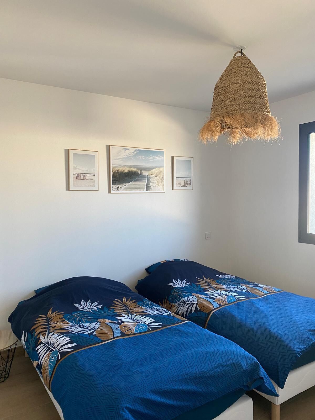 A bedroom with two beds, a hanging light fixture, and three framed pictures on the wall.