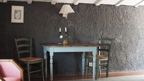 Um quarto com parede de pedra rústica, uma mesa de madeira com duas cadeiras, um quadro emoldurado e uma luminária na parede.