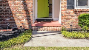 Uma casa com fachada de tijolos, porta verde e um pequeno jardim frontal.
