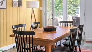 Uma sala de jantar com mesa de madeira e cadeiras pretas, ventilador de teto e vista para um pátio externo através de portas de vidro.
