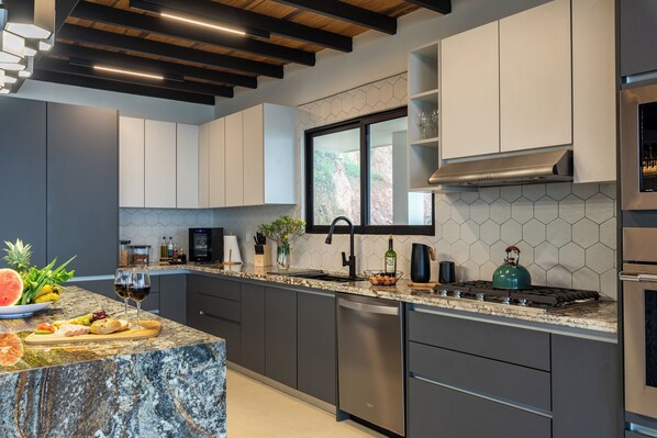 A modern kitchen with dark grey cabinets, a stainless steel dishwasher, a gas stove, and a large window providing natural light. - Lumina Valley View Monteverde (Monteverde)