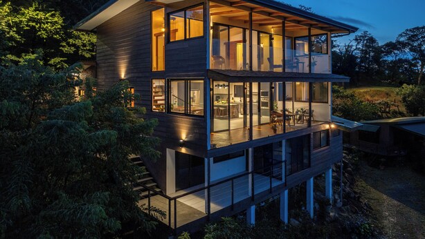 Une maison moderne à plusieurs étages, dotée de grandes fenêtres, d’un balcon et d’un espace cuisine ouvert.