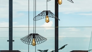 Un intérieur moderne avec des luminaires suspendus, de grandes fenêtres et deux chaises en bois.