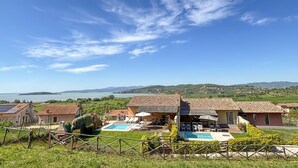 Een villa met zwembad, omringd door weelderige begroeiing en uitzicht op zee en heuvels.