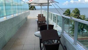 A balcony with glass railings, outdoor seating, and a view of the ocean.