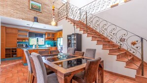 Eine moderne Küche mit Holzschränken, einem Esstisch mit Stühlen und einer Treppe mit aufwendiger Geländerarbeiten.