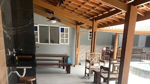 A covered outdoor area with a pool, wooden benches, and a bar area with stools. - Happy Corner Cottage  (Chácaras Mogiano Bertioga)