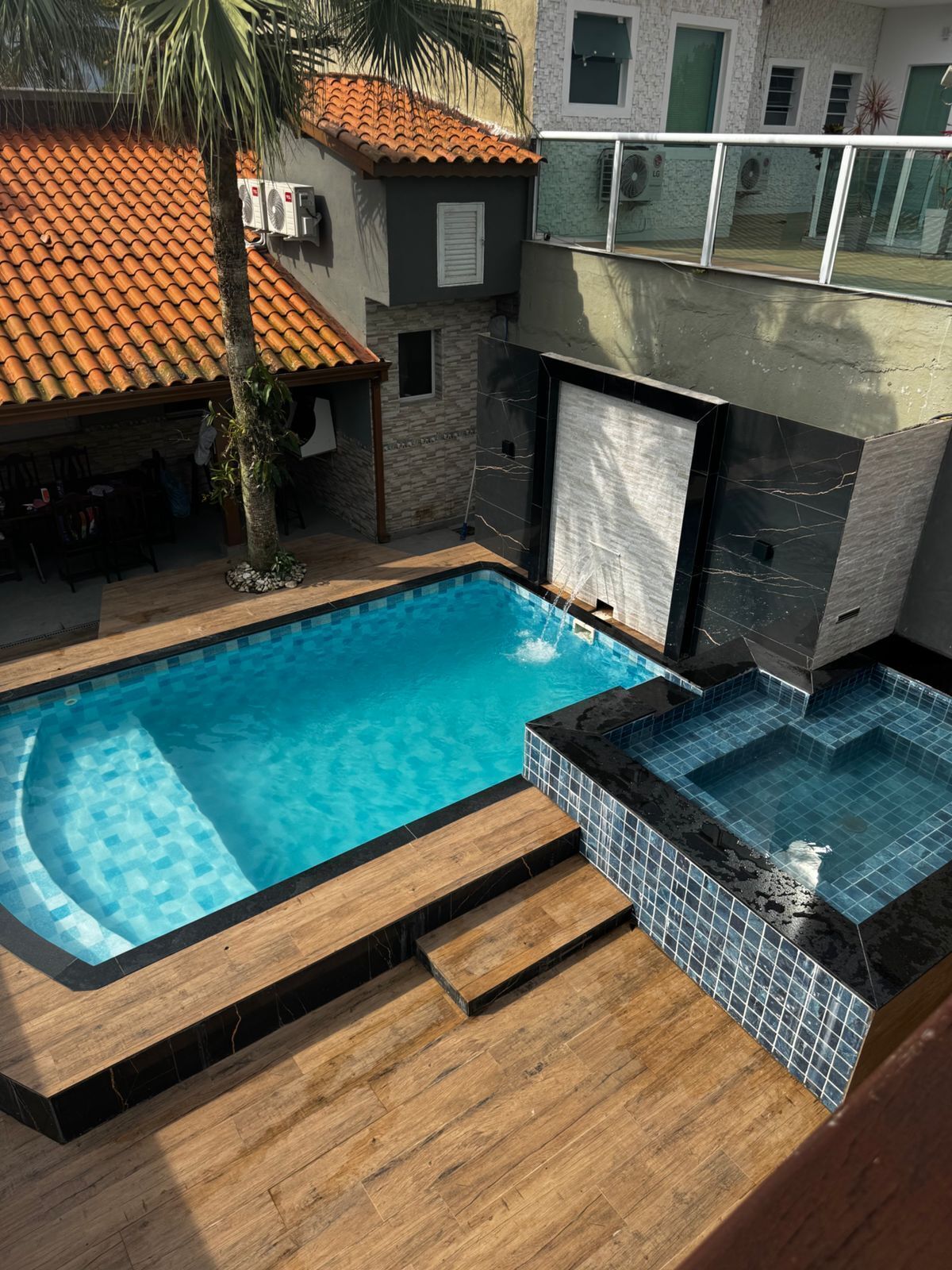 A swimming pool with a wooden deck and a small jacuzzi area.