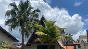 A residential property with a stone pathway, palm trees, and a house with a tiled roof. - Happy Corner Cottage  (Chácaras Mogiano Bertioga)