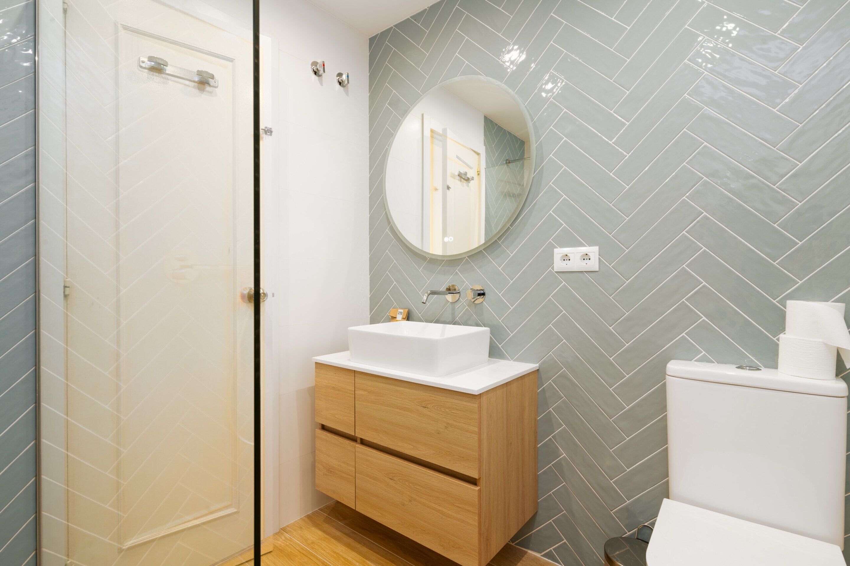 Een badkamer met een wit wastafel, houten wastafelmeubel, een spiegel en een toilet.