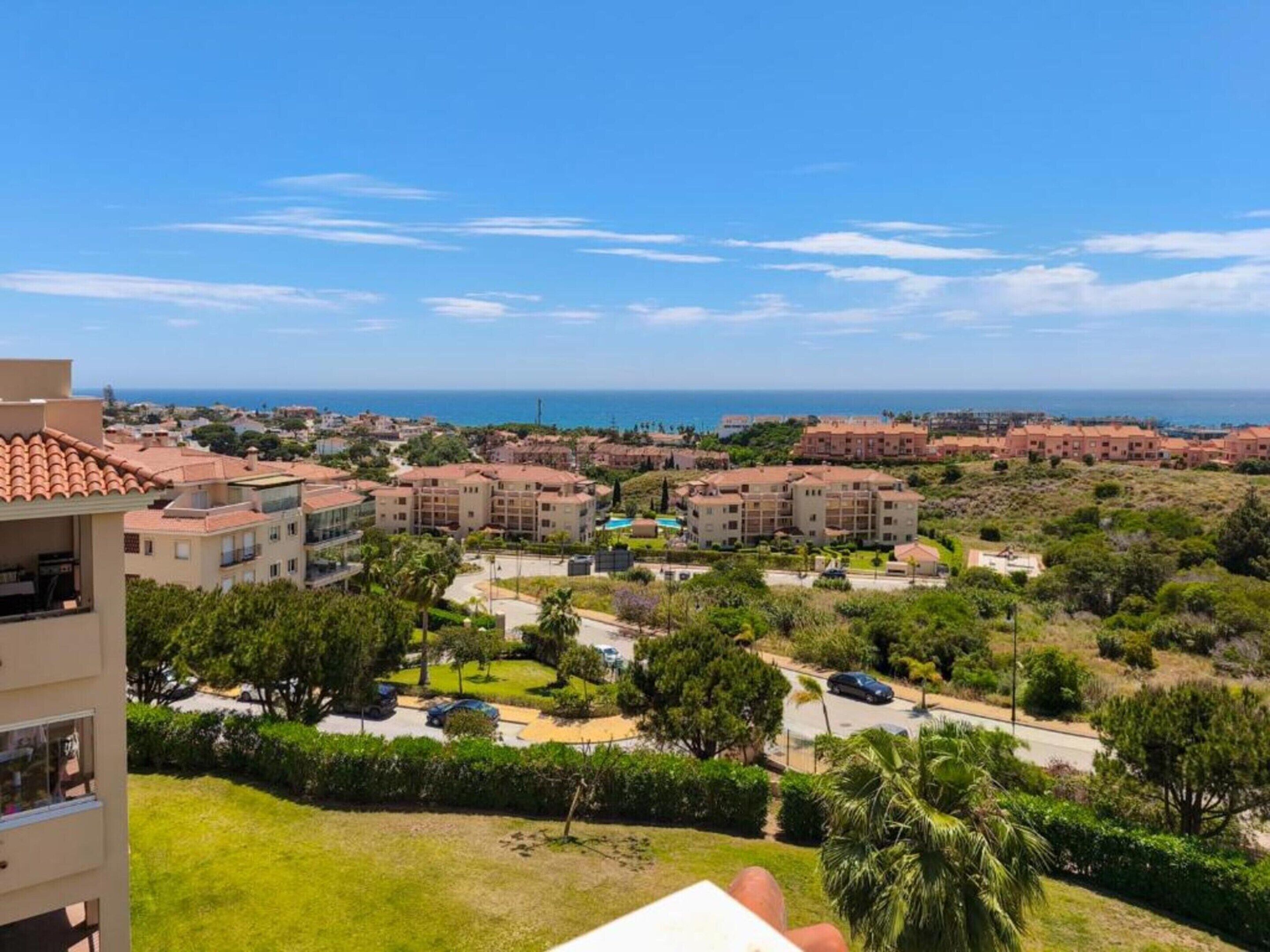 A coastal residential area with multiple apartment buildings, a clear blue sky, and a view of the sea.