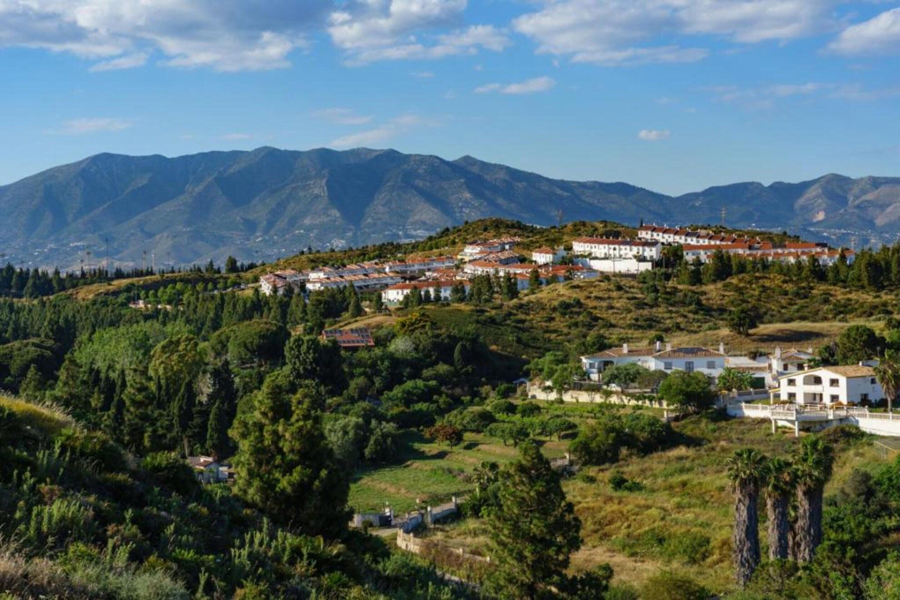 A hillside village with traditional white buildings and red-tiled roofs, surrounded by lush greenery and mountains.