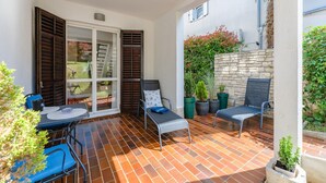 Patio con tavolo, due sedie, una porta scorrevole in vetro e piante in vaso.
