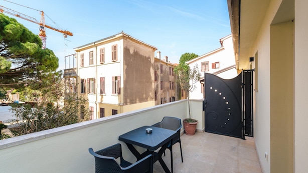 A balcony with a table and chairs, a potted plant, and a view of buildings and a crane in the background. - Apartment With View (Porec)