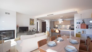 Una sala moderna con chimenea, un comedor con mesa preparada para cuatro personas y una cocina al fondo.