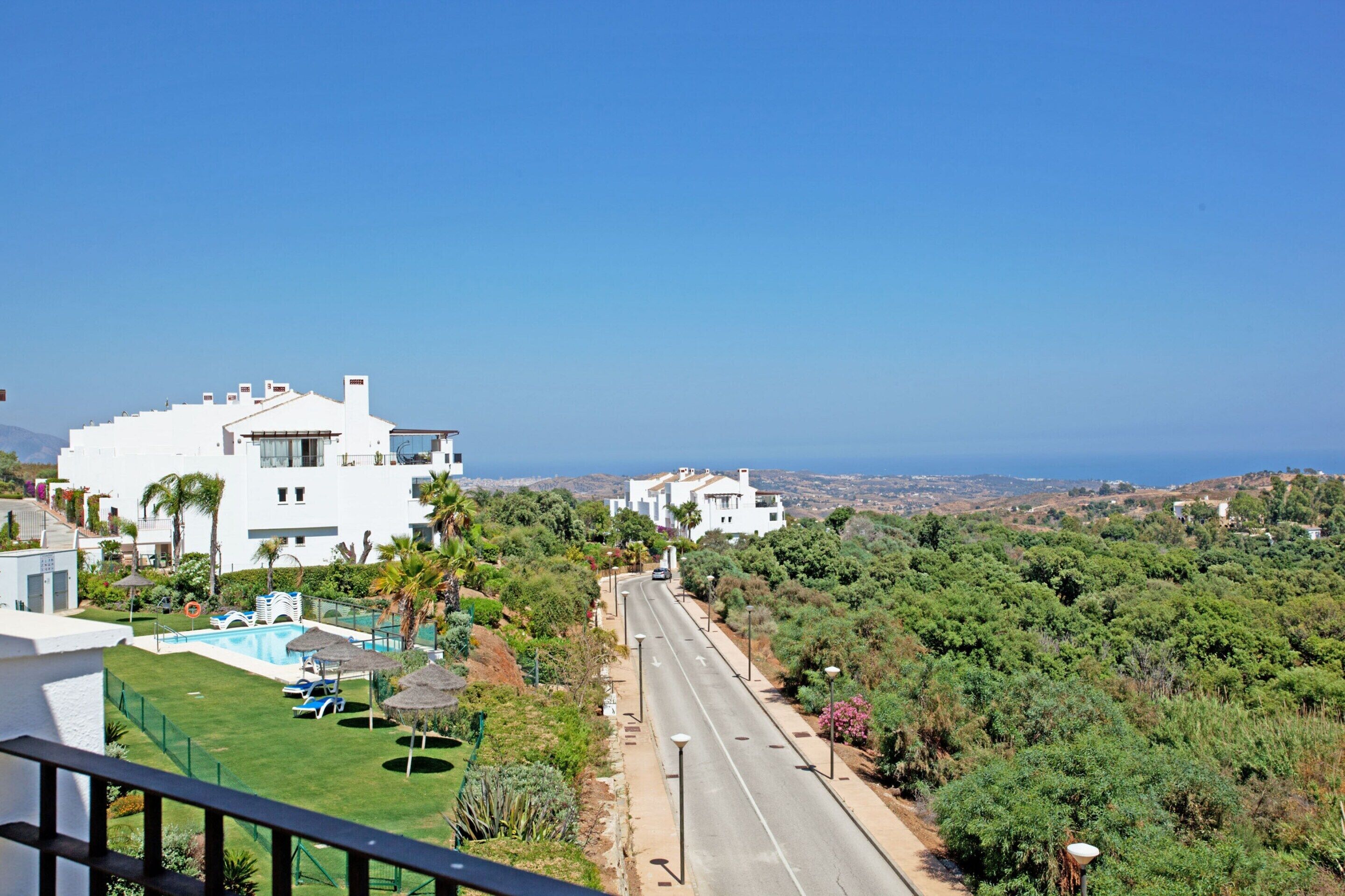 A residential area with white houses, a swimming pool, and a road.