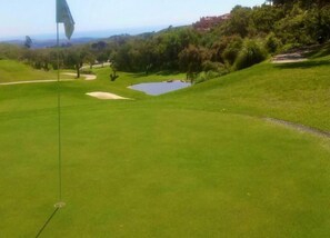 A golf course with a flag, a pond, and a hilly landscape. - Sunny Terrace Apartment (Ojén)