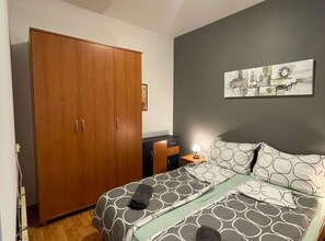 A bedroom with a large wardrobe, a bed with patterned bedding, a nightstand with a lamp, and a wall-mounted painting. - Comfortable Apartment With Terrace (Porec)
