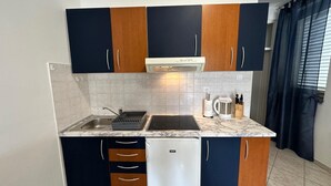 A compact kitchen with dark cabinets, a white refrigerator, a built-in oven, and a sink.