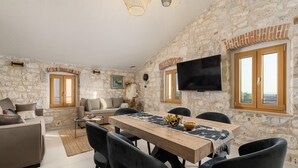A spacious living area with a stone wall, a wooden dining table, and modern furniture. - Beautiful Apartment With View (Porec)