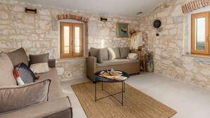 A living room with stone walls, a sofa, a wicker chair, and a small table. - Beautiful Apartment With View (Porec)