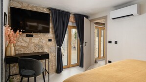A bedroom with a bed, a desk, a chair, a TV, and a stone wall. - Beautiful Apartment With View (Porec)