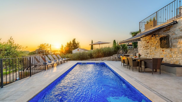 A rectangular swimming pool with a stone wall on one side, surrounded by lounge chairs and a dining area with outdoor furniture. - Beautiful Apartment With View (Porec)