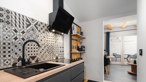 A modern kitchen with a geometric tile backsplash, a black faucet, and a flat-screen TV mounted above the counter. - Apartment With Scenic View (Porec)