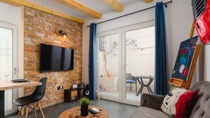 A modern living room with a brick wall, a flat-screen TV, a dining area with a table and chairs, and a large window with curtains. - Apartment With Scenic View (Porec)