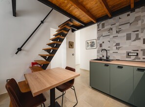 A modern kitchen with a wooden staircase, a dining area with a wooden table and chairs, and a patterned wall. - Apartment With Cozy Bedroom (Porec)